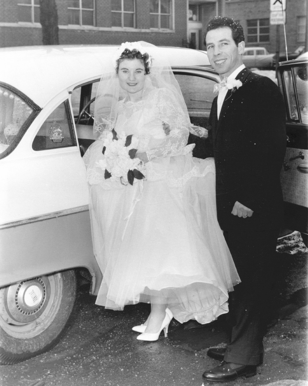 Photo en noir et blanc d’un homme et d’une femme italiens qui montent dans une voiture le jour de leur mariage.