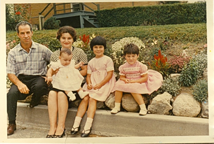Vieille photo d’une famille italienne composée d’un homme, d’une femme et de trois enfants, tous bien habillés et assis dehors.