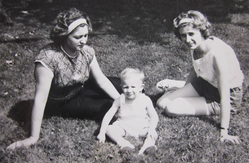 Un jeune garçon est assis sur l’herbe avec deux femmes assises à côté de lui,