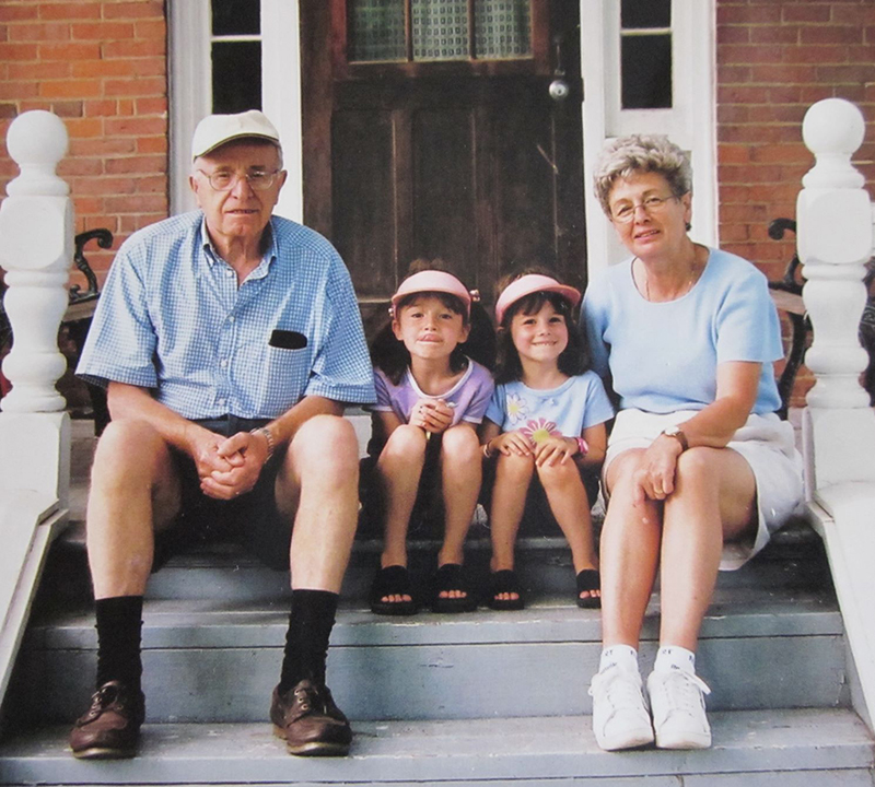 Deux petites filles s’assoient sur les marches d’une maison avec leurs grands-parents à côté d’elles.