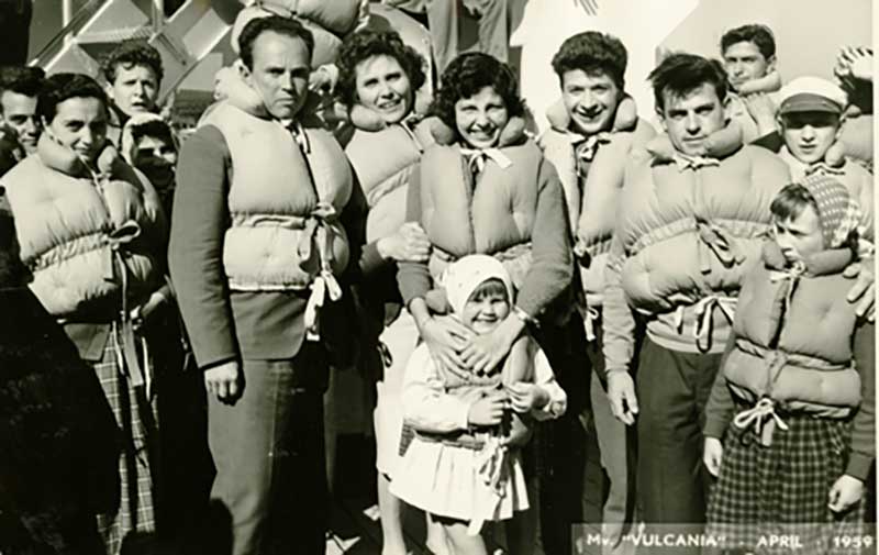 Un groupe d’adultes et d’enfants debout sur le pont d’un navire; ils portent tous des vestes de sauvetage.
