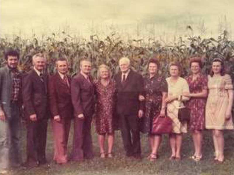 Neuf membres de la famille étant debout sur herbe, avec champ de blé en arrière-plan