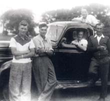Cinq jeunes hommes dans et autour d’une vieille voiture modèle.