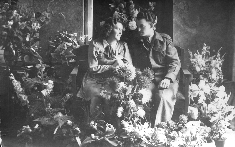 Photo en noir et blanc d’un beau couple assis parmi des fleurs.