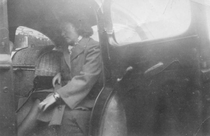 Photo en noir et blanc d’une dame assise dans une voiture avec beaucoup d’articles.