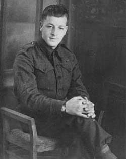 Jeune homme en tenue militaire, assis sur une chaise, les mains jointes autour d’un genou.
