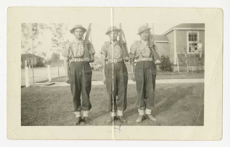 Trois jeunes hommes en uniforme militaire tiennent un fusil sur leur épaule gauche.