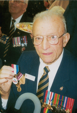 Photo en couleur d’Ernest, un homme âgé, montrant fièrement ses médailles.