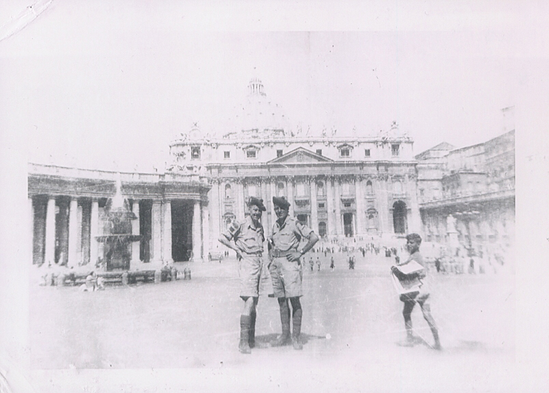 Deux hommes en uniforme militaire se tiennent sur une place avec une grande église derrière eux.