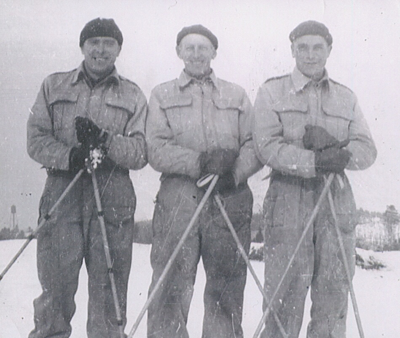 Trois hommes portant des vêtements d’hiver se tiennent côte à côte, chacun tenant des bâtons de ski.
