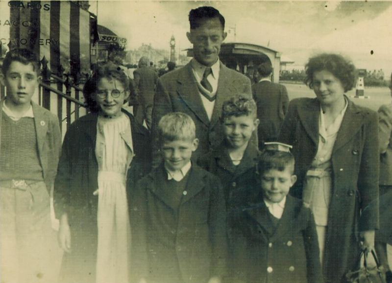 Vieille image en noir et blanc d’un couple avec leurs cinq enfants debout devant eux.