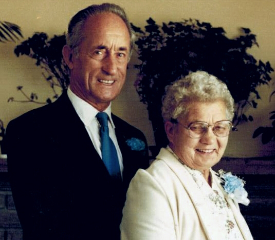 Un couple bien-habillé sourire à la caméra, la femme porte un corsage bleu.