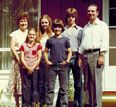 Un homme et une femme debout sur la pelouse devant leur maison, quatre enfants se tiennent entre eux.