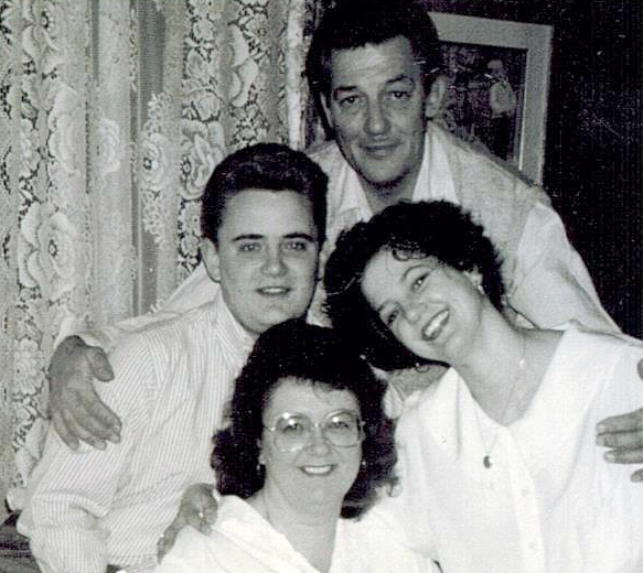 Vieille photo en noir et blanc d’une famille de quatre personnes, souriant pour la caméra.