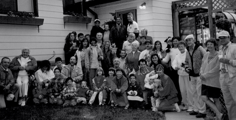 Un très grand groupe d’hommes, de femmes et d’enfants debout devant une maison, tous regardant la caméra et souriant.