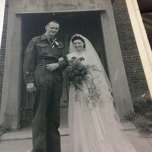 Couple nouvellement marié est debout en face de l’immeuble, avec la mariée tenant des fleurs.