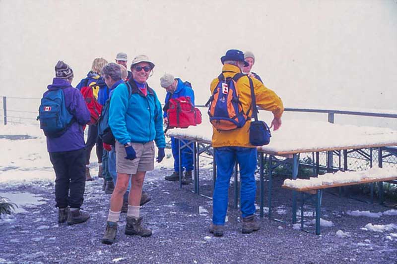 Un groupe de randonneurs se tient devant une table extérieure, il y a de la neige dessus.