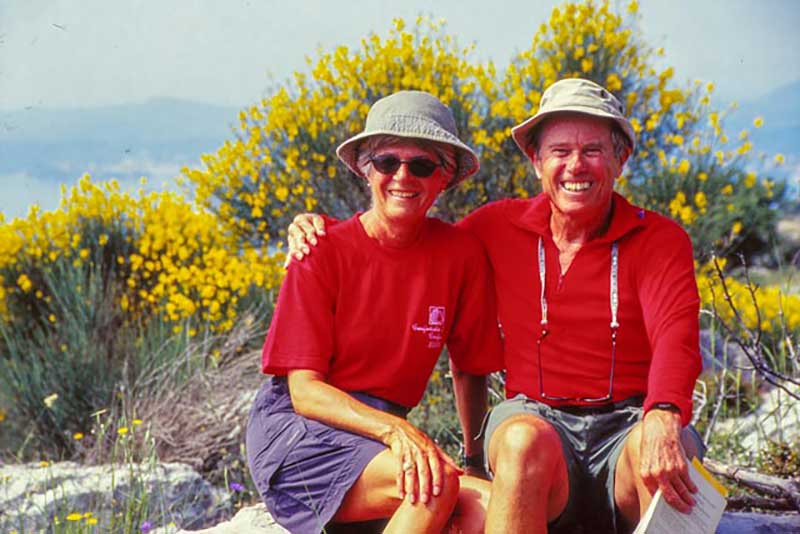 Un homme et une femme en t-shirts rouges et chapeaux assortis s’assoient et sourient à la caméra.