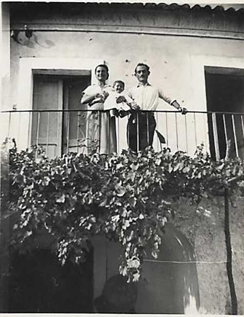 Homme, femme et bébé se penchent contre une balustrade et regardent vers le bas de leur balcon.