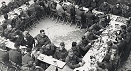 Groupe d’hommes en uniforme assis sur les tables.