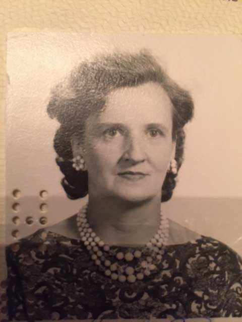 Une femme portant des perles et des boucles d’oreilles est assise pour faire prendre sa photo de passeport.