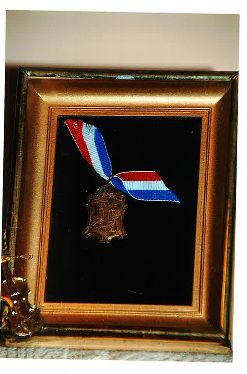 Une médaille d’or en forme de violons est dans un cadre, avec un ruban rouge, blanc et bleu attaché.