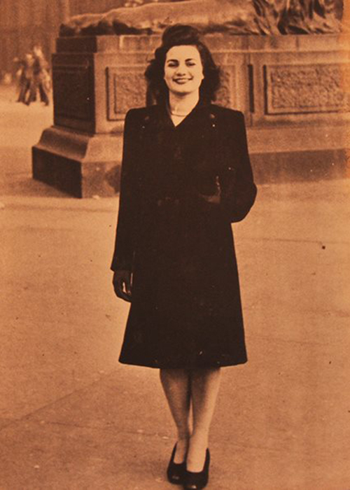 Sepia photo d’une jeune femme en manteau noir debout devant une statue.