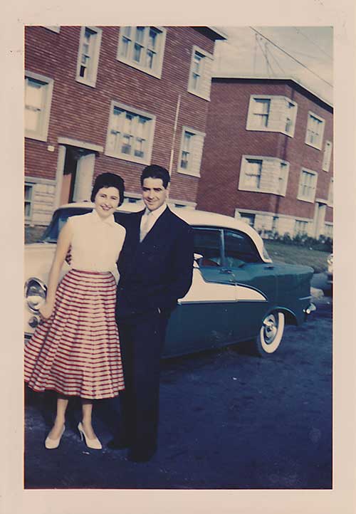 Homme et femme debout devant une vieille voiture.