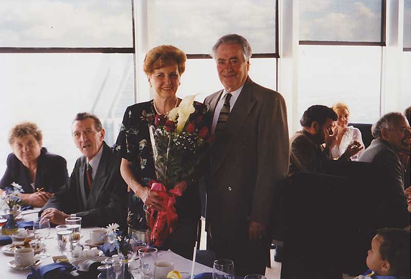 Homme et femme debout devant une table, la femme tient un bouquet de fleurs.