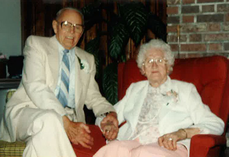 Vieille femme aux cheveux blancs assise sur un canapé rouge et l’homme est assis à côté d’elle et lui tenant la main.