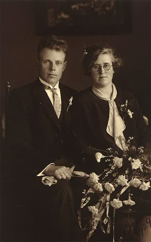 Homme et femme portant des vêtements noirs assis sur une chaise, la femme a des fleurs sur ses genoux.