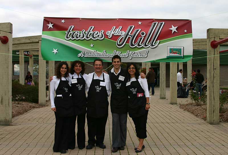 Cinq membres d’une famille portant des tabliers devant un panneau indiquant « Tastes of the Hill ».