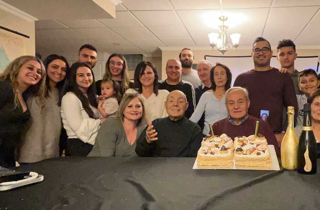 Une grande famille est assise autour d’un homme âgé, qui a un gâteau d’anniversaire en face de lui.
