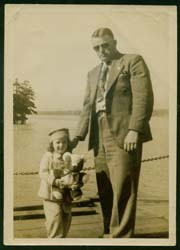 Gerald portant des lunettes de soleil, debout avec sa jeune fille tenant un ours en peluche. 