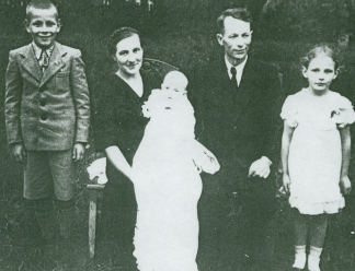 Karline tenant bébé Ausma dans sa robe de baptême, avec sa famille à ses côtés.
