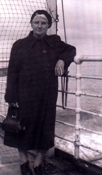 Femme en vêtement et chapeau noirs, un coude sur la balustrade d’un bateau.