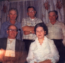 Photographie couleur d’un homme et d’une femme, assis, trois hommes debout derrière eux.