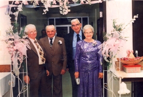 Femme plus âgée en robe mauve, debout avec trois hommes en costume.