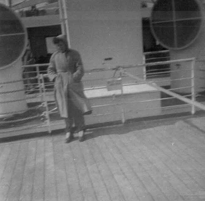 L’homme est debout sur le pont supérieur du navire, tenant son manteau.