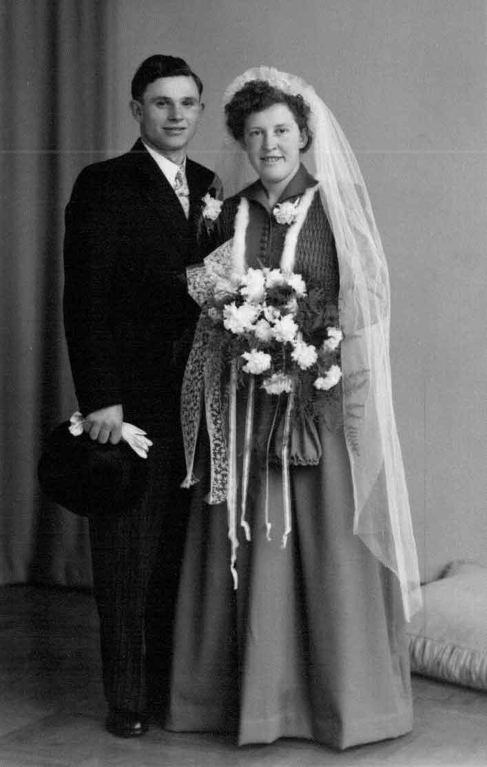 Couple en robe de mariée debout devant le mur tenant des fleurs à la main.