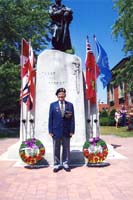 Henry est un homme plus âgé, debout devant le monument avec des couronnes et des drapeaux à côté.