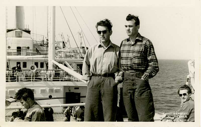 Deux jeunes hommes, côte à côte sur le pont d’un navire.