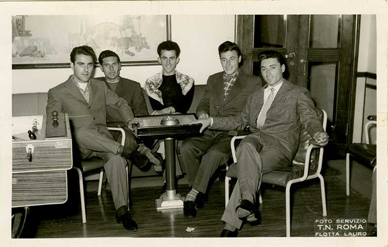 Cinq jeunes hommes assis autour d’une table. Ils posent pour une photographie professionnelle.