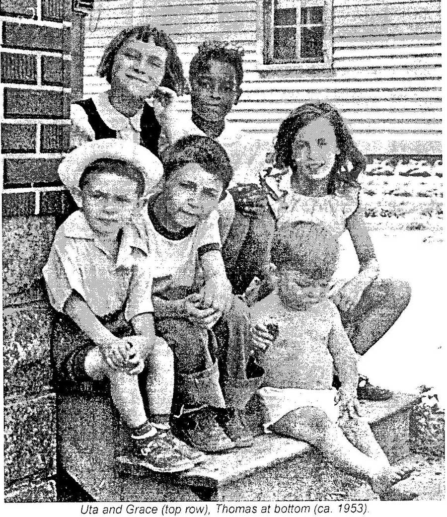 Photo en noir et blanc de six enfants assis dehors sur des marches, souriant à la caméra.