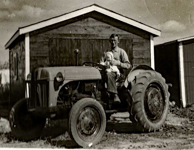 Un jeune homme tient un bébé assis sur un tracteur.