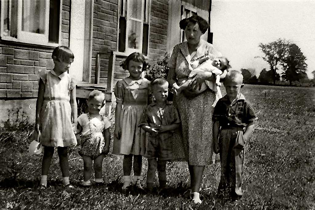 Une jeune femme se tient sur l’herbe avec cinq petits enfants et un bébé.