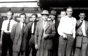 Vieille photographie de plusieurs hommes debout en costumes, cravates et chapeaux.