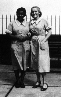 Deux femmes en tenue d’infirmière, debout devant une clôture en fer.