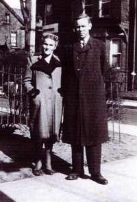 Homme et femme en manteaux, debout au coin d’une rue.