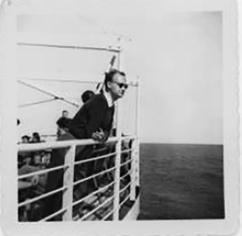 Un homme portant des lunettes soleil qui se penche contre la rambarde d’un navire.